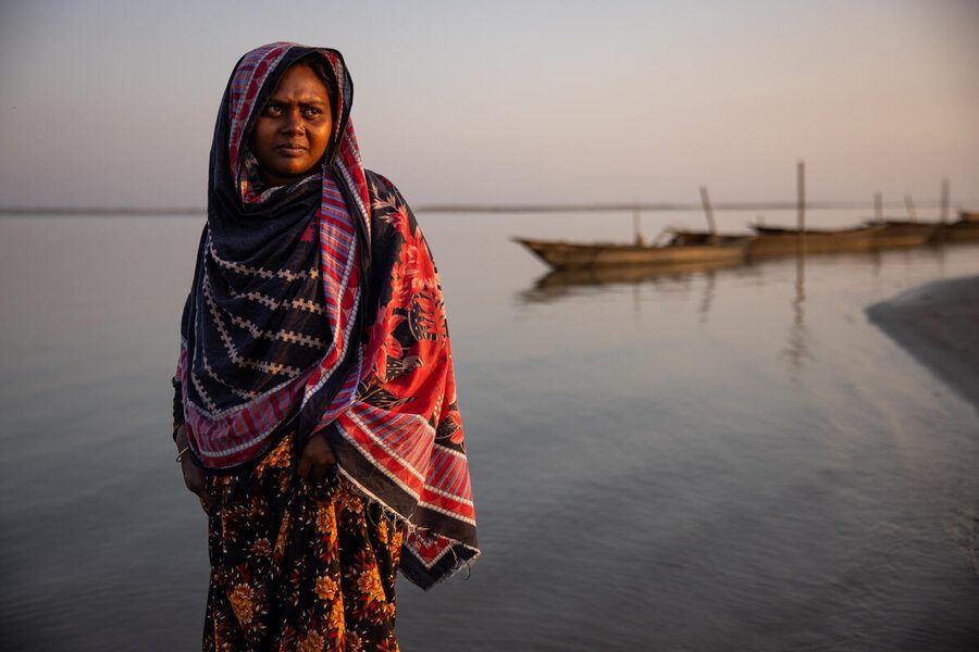 In this photo Parul poses for a portrait at her home in the Kurigram district of Bangladesh. Her home has been newly raised to help prevent it from being flooded.  Parul lives with her parents, two brothers, and her two young sons on a sand island (called a ‘char’ in Bengali) in Kurigram district in northern Bangladesh – one of the poorest areas of the country. A single mother, Parul does various activities to support her children, from farming vegetables (gourds and beans) to raising livestock. Flooding has been a constant source of worry in her life – until 2024, when WFP raised the small strip of land her village sits on.  In the past, Parul received anticipatory cash payouts from WFP ahead of floods, which she used to buy dry food and medicine to keep her family alive, but she couldn’t save her crops or the animals she raises. When seasonal flooding caused the waters around her village to rise, Parul had to build and live on a raft with her two little boys, terrified they would fall into the water and drown. Now her family and her livestock are protected – and therefore her food security. Parul dreams of educating her sons so they can get good jobs and have a better life – although she worries about being able to afford to send them past primary school, due to her limited income. Besides being a talented cook, she is a passionate ‘Kantha’ (quilted blanket) maker. “If my house was still down there, this year’s flood would have sunk it,” says Parul. “We would have been swept away by the tides. Thank God that through WFP we got a raised house. Moving up here we are in a much better place.”Low-lying Bangladesh counts among one of the world’s most at-risk countries to climate disasters. The 2024 cyclone and monsoon season affected nearly 20 million people countrywide, deepening hunger that already grips more than one-fifth of the population.  Northern Bangladesh is a flood-prone region with seasonal flooding varying in intensit